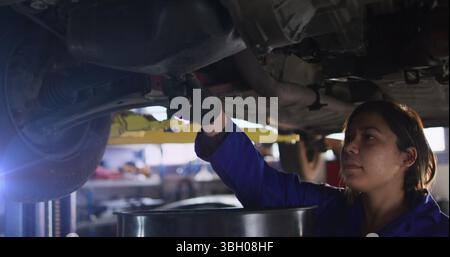 Bild einer weiblichen asiatischen Mechanikerin im mittleren Erwachsenenalter, die Motoröl aus dem Auto in der Garage ablässt Stockfoto