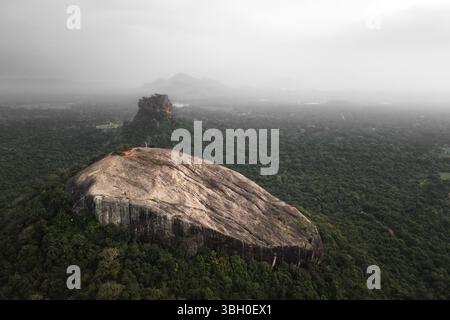 Besucher aus der Vogelperspektive wandern auf dem Pidurangala Rock mit Blick auf den Sigiriya Rock und den üppigen grünen Dschungel im Sri Lanka Cultural Triangl Stockfoto
