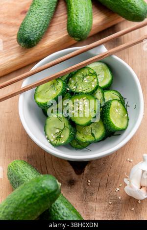 Sunomono, japanischer Gurkensalat. In Scheiben geschnittene Gurken mit asiatischem Dressing aus Sojasauce, Reisessig, Sesamöl, Zucker und Dill in einer weißen Schüssel auf Holz ta Stockfoto