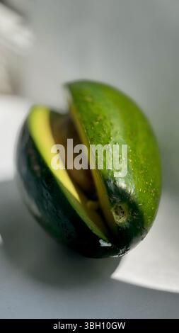 Nahaufnahme einer geschnittenen Reifen Avocado, die den Samen freilegt, auf einer sauberen weißen Oberfläche mit natürlichem Licht und Schatten. Stockfoto