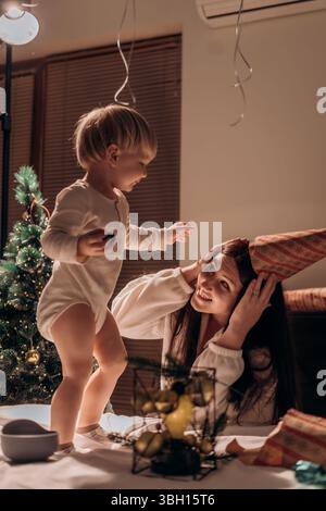 Ein herzlicher Moment der Feier, bei dem Mutter und Kind gemeinsam einen festlichen Baum schmücken Mutter und Sohn gemeinsam den Winterurlaub feiern Stockfoto