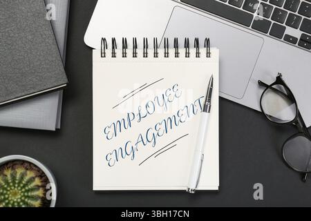 Emotionale Mitarbeiterbindung. Wörter in Notizbuch, Stift und Laptop auf schwarzem Tisch, Draufsicht Stockfoto