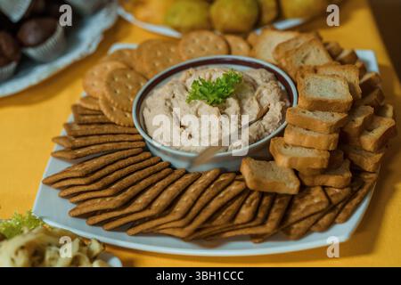 Eine wunderschön angeordnete Wurstplatte bietet einen cremigen Lachsdip, umgeben von verschiedenen Crackern, Brot und Schokoladengerichten, perfekt für Partys Stockfoto
