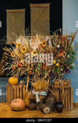 Eine warme herbstliche Stillleben-Szene mit Sonnenblumen, getrocknetem Weizen und Kürbissen, die auf Holzkisten und Baumstämmen angeordnet sind, schafft eine gemütliche Ernteatmosphäre Stockfoto