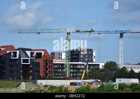 Neues Wohngebäude im Bau mit zwei großen Turmdrehkranen und einem Autokran vor Ort. Stadtentwicklung und Immobilienwachstum sce Stockfoto
