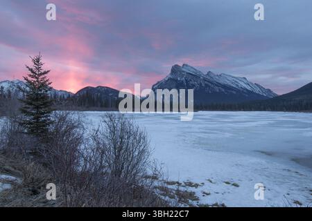 Ein leuchtend rosa Sonnenstrahl erleuchtet den Himmel hinter dem gefrorenen Vermillion Lake Bergmassiv Stockfoto
