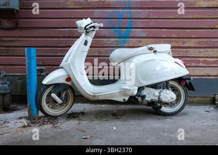 Ein weißer Vespa-Roller ist an einem Posten in Vancouver, BC, mit einem Vorhängeschloss gesichert. Stockfoto