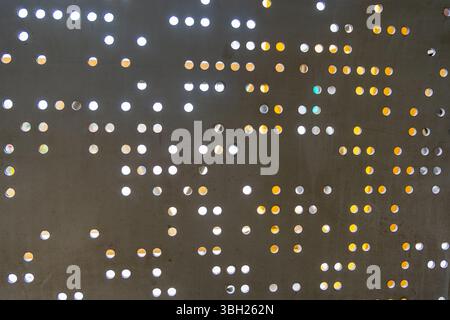 Muster von schwarzen und weißen Punkten an einer Wand. Die Punkte sind in einem Raster angeordnet, wobei einige größere und andere kleinere Punkte aufweisen. Der Gesamteffekt ist etwas abstra Stockfoto
