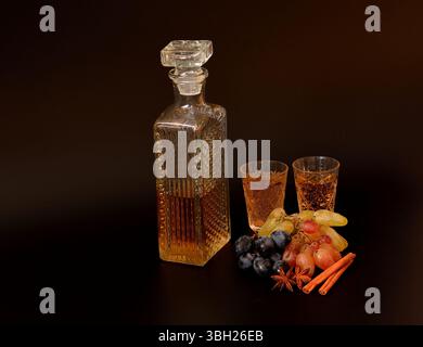Grappa mit Gewürzen in Kristallglas auf schwarzem Hintergrund, reife Trauben verschiedener Sorten in der Nähe. Stockfoto