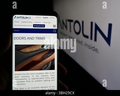 In dieser Fotoabbildung hält eine Person ein Handy mit der Webseite des spanischen Automobilunternehmens Grupo Antolin vor dem Logo. Stockfoto