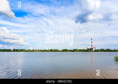 Weitwinkelansicht einer Abfallverbrennungsanlage neben einem ruhigen See in Kiew mit Wolken, die sich unter blauem Himmel im Wasser spiegeln. Stockfoto