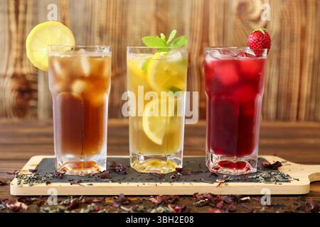 Drei große Gläser mit erfrischenden Getränken stehen auf einem Holztisch. Eistee mit Zitronenscheibe, Zitronengetränk mit frischer Minze und Fruchtpunsch mit Erdbeeren. Stockfoto