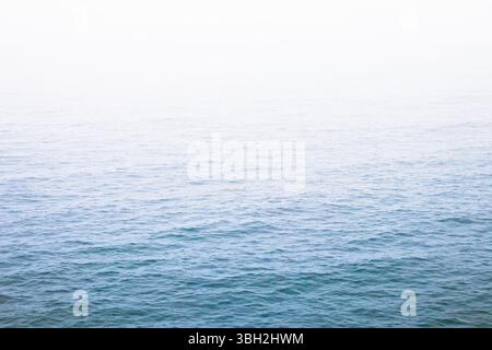 Sanfte blaue Wellen verströmen an der Pazifikküste in Oceanside, Kalifornien, in einen hellen, nebeligen Horizont. Ruhige, minimale Meereslandschaft, ideal für Hintergründe oder Sere Stockfoto