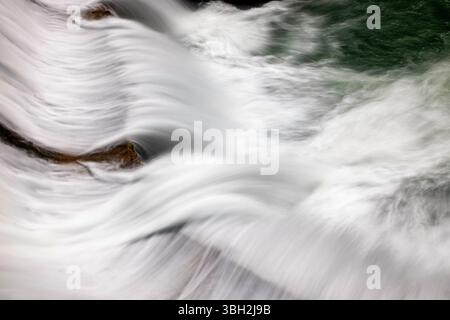 Lange Exposition von rauschendem Wasser, das über Felsen in einem Fluss fließt, erzeugt glatte, seidige Bewegungen und natürliche Muster in einer dynamischen und ruhigen Landschaft Stockfoto
