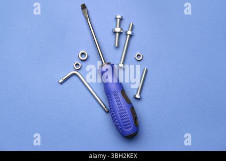 Gewindebolzen, Chrommuttern und Schraubendreher auf blauem Hintergrund Stockfoto