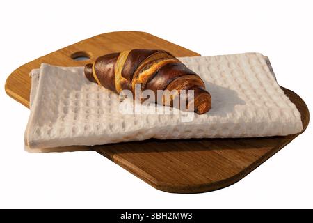 Frisch gebackenes Schokoladencroissant auf einem gefalteten weißen Handtuch auf einem hölzernen Schneidebrett. Leckeres Gebäck-Konzept mit sanftem Morgenlicht und c Stockfoto