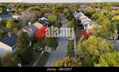 Von Bäumen gesäumte Wohnstraße im Herbst. Ein malerischer Blick aus der Luft auf eine Wohnstraße, gesäumt von Häusern, bunten Herbstbäumen und gepflegt Stockfoto