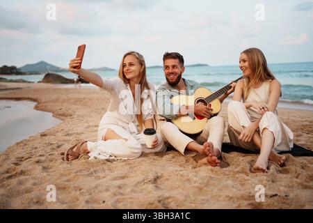 Glückliche Freunde, die am sonnigen Sommertag mit Gitarre am Strand rumhängen Stockfoto