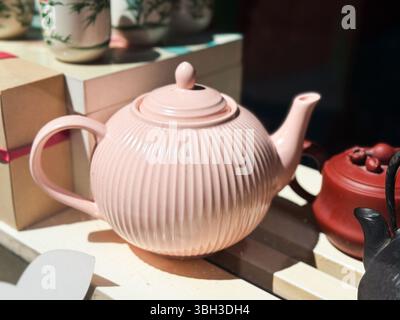 Rosafarbene Keramik-Teekanne im Sonnenlicht. Gerippte Teekanne mit anderen traditionellen Teeartikeln. Stockfoto