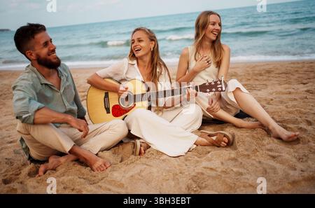Freunde hängen an einem warmen Sommertag mit Gitarre am Strand ab Stockfoto