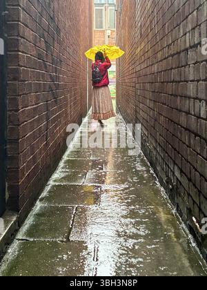 Exeter, Devon, Großbritannien. Juni 2025. Wetter in Großbritannien: Starker Regen in Exeter, Devon. Im Bild: Frau kämpft an einem nassen und regnerischen Tag in Exeter mit einem gelben Regenschirm in der schmalen Parlamentsstraße, der schmalsten Straße Großbritanniens. Hinweis: Nidpor/Alamy Live News Stockfoto