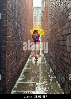 Exeter, Devon, Großbritannien. Juni 2025. Wetter in Großbritannien: Starker Regen in Exeter, Devon. Im Bild: Frau kämpft an einem nassen und regnerischen Tag in Exeter mit einem gelben Regenschirm in der schmalen Parlamentsstraße, der schmalsten Straße Großbritanniens. Hinweis: Nidpor/Alamy Live News Stockfoto