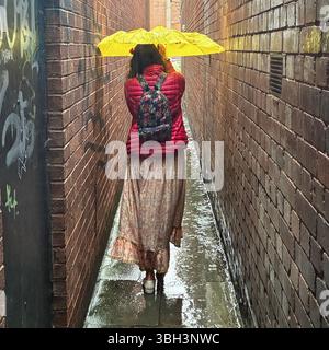 Exeter, Devon, Großbritannien. Juni 2025. Wetter in Großbritannien: Starker Regen in Exeter, Devon. Im Bild: Frau kämpft an einem nassen und regnerischen Tag in Exeter mit einem gelben Regenschirm in der schmalen Parlamentsstraße, der schmalsten Straße Großbritanniens. Hinweis: Nidpor/Alamy Live News Stockfoto