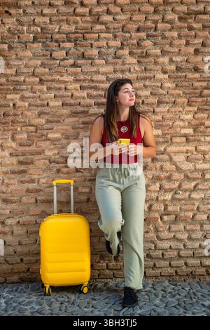 Mädchen mit Handy in beiden Händen, legt ihren Fuß auf eine alte Ziegelwand und schaut zur Seite, als ob etwas sie aufmerksam machen würde. Sommer-STYLE, Typ Stockfoto