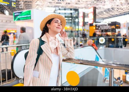 Lächelnde junge Kaukasierin mit Strohhut und Rucksack. Passagier, der am Flughafen auf dem Flug wartet. Urlaub und Urlaub. Stockfoto