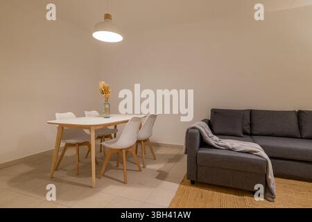 Seitenwinkel des Essbereichs mit weißem Tisch und vier Stühlen neben dem Wohnzimmer und Sofa Stockfoto