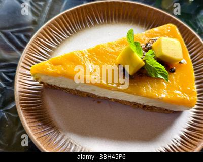 Eine Scheibe Mango-Käsekuchen mit Crackerkruste, cremiger Käseschicht, Mangoblaze-Belag, garniert mit frischen Mangowürfeln und Minze Stockfoto