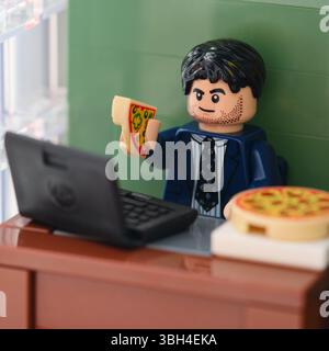 Tambow, Russische Föderation - 17. Februar 2025 Lego-Geschäftsmann sitzt hinter einem Tisch mit Laptop drauf in einem Büro und isst Pizza. Nahaufnahme Stockfoto