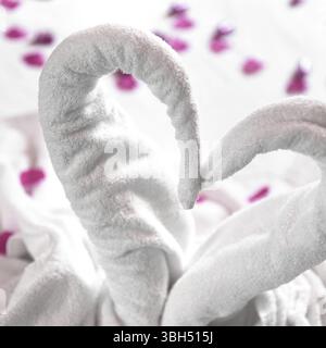 Zwei Handtuchschwäne auf dem Bett, mit rosa Blütenblättern bestreut. Das Handtuch sieht aus wie Herzform und es ist für Paar in Honigmond vorzubereiten. Ideal für Veranstaltungen und Stockfoto