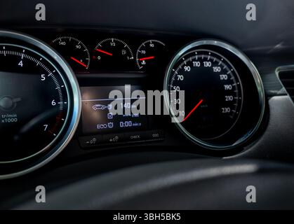 Detailansicht eines modernen Armaturenbretts mit beleuchtetem Drehzahlmesser, Tachometer, Kraftstoffanzeige und zentralem Digitalbildschirm mit ECO-Modus und Reichweite in Stockfoto
