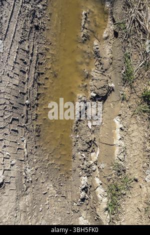 Reifenspuren auf einer schlammigen Straße auf dem Land. Pfützen in den Gruben einer Feldstraße Stockfoto