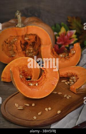 Ganzer frischer, großer, orangefarbener Kürbis und ein Stück Kürbis auf Holzbrett, Nahaufnahme. Bio-pflanzliches Produkt, Zutaten zum Kochen, gesundes Essen vegan Stockfoto