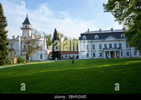 Ein großes weißes Haus mit einem roten Dach befindet sich vor einem großen grünen Feld. Ein paar Leute spielen auf dem Spielfeld Stockfoto