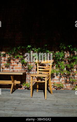 Holzstuhl sitzt auf einer Holzbank vor einer Ziegelwand. Der Stuhl ist leer, und die Bank ist auch leer. Die Szene ist ruhig und friedlich Stockfoto