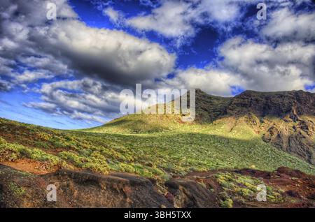 Wolken am blauen Himmel und grüne Felder mit Bergen am sonnigen Tag, Nordwestküste Teneriffas in der Nähe des Leuchtturms Punto Teno, Canaria Stockfoto