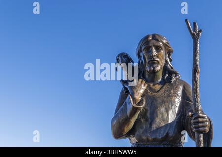 Antike Bronzestatue von Jesus Christus, dem Guten Hirten, mit dem verlorenen Schaf auf seinen Schultern, isoliert auf einem blauen Himmel Hintergrund. Leerzeichen für Text Stockfoto