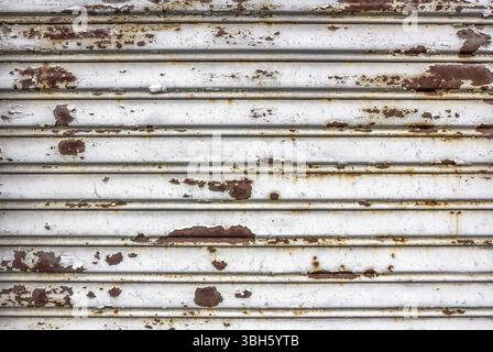 Alte beschädigte weiße Rollstahltür. Ein Verschluss ist total verrostet, seit Jahren geschlossen Stockfoto