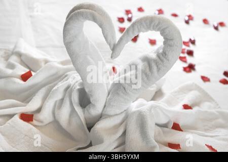 Weiß zwei Handtuch Schwäne auf dem Bett, bestreut mit roten Blütenblättern. Das handtuch aussehen wie Herz und Es ist für die Paare, die in der Honig Mond vorzubereiten. Ideal für selbst Stockfoto