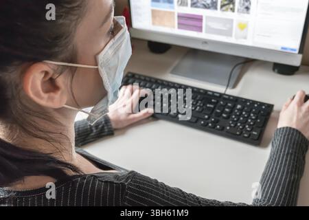 Junge Geschäftsfrau, die von zu Hause aus mit Schutzmaske arbeitet. Coronavirus. Geschäftsfrau in Quarantäne für Coronavirus mit Schutzmaske. Wor Stockfoto