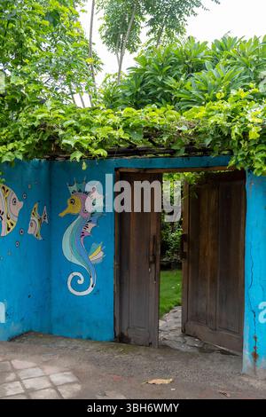 Gili Trawangan, Indonesien - 4. Januar 2025: Blaue Wand mit einem Seepferd und zwei Fischen darauf gemalt. Die Tür ist offen und dahinter befindet sich ein Holzzaun Stockfoto