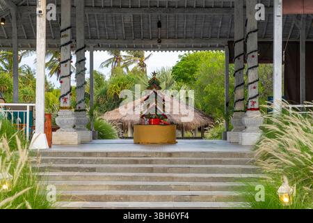 Weihnachtsbaum aus Holzstäbchen steht auf einer Bühne. Der Baum ist mit Lichtern und Geschenken dekoriert. Die Bühne ist von Palmen und einer Hütte umgeben. T Stockfoto