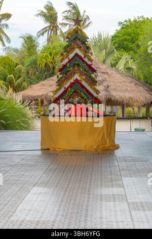 Weihnachtsbaum aus Holzstäbchen steht auf einer Bühne. Der Baum ist mit Lichtern und Geschenken dekoriert. Die Bühne ist von Palmen und einer Hütte umgeben. T Stockfoto