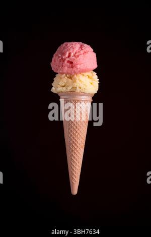 Studio-Aufnahme eines Eiskegels mit zwei Schaufeln und Erdbeeren- und Vanillearomen, isoliert vor einem dramatischen schwarzen Hintergrund. Perfekt zum Nachtisch Stockfoto