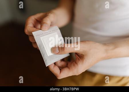 Nahaufnahme der Hände eines nicht erkennbaren Mannes, der einen Tropfkaffeesack hält und sich morgens auf die Zubereitung einer frischen Tasse aromatischen Kaffees zuhause vorbereitet. Stockfoto