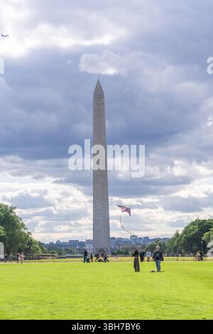 Washington D.C., USA, - 23. Mai 2025 versammeln sich Menschen in der Nähe des Washington Monuments, während ein farbenfroher Drachen unter einem teilweise bewölkten Himmel in der Brise fliegt. Stockfoto