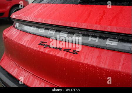 Ein roter Porsche Taycan 4S parkt im Regen. Die Rückseite des Fahrzeugs ist nass und das Logo ist sichtbar Stockfoto